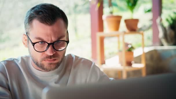 Egy szemüveges fiatalember, aki a laptop képernyőjére néz. — Stock videók