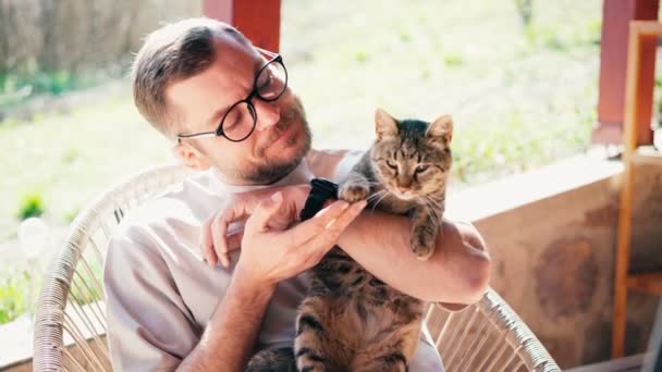 Um homem barbudo atraente usando óculos abraçando seu gato cinza bonito — Vídeo de Stock