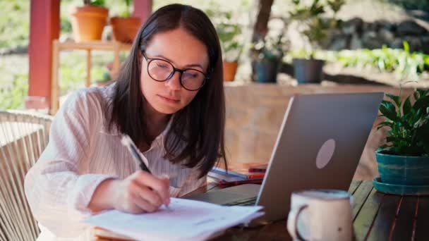 Uma jovem freelancer faz anotações em um caderno e um laptop — Vídeo de Stock