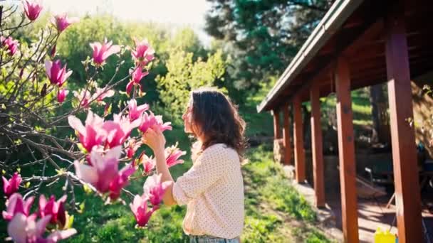 En vacker ung kvinna njuter av doften av rosa magnolia blommor — Stockvideo