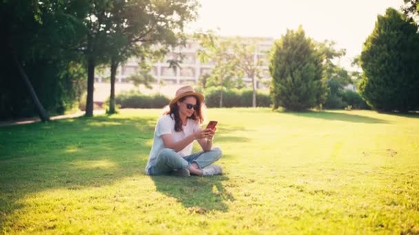 Молодая Женщина Солнечных Очках Плетеной Шляпе Использует Свой Телефон Сидя — стоковое видео