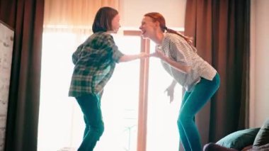 Mutlu bir anne ve kızı, müzik dinlerken yatakta zıplayarak ve dans ederek eğleniyorlar.