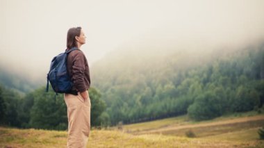 Sırt çantalı bir insan sonbaharda sisle kaplı dağların güzel manzarasının tadını çıkarıyor..