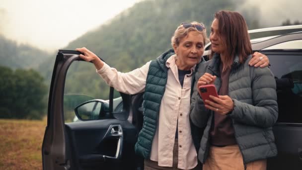 一位年长的高加索妇女和她的成年女儿站在汽车旁边用智能手机 — 图库视频影像