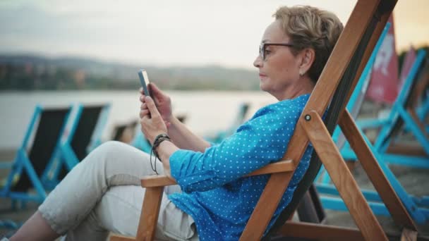 Nehir Kıyısında Plaj Sandalyesinde Otururken Akıllı Telefonunu Kullanan Son Sınıf — Stok video