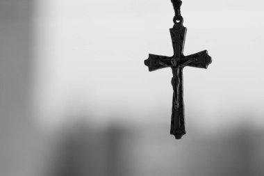 Üzgün, bulutlu, fakir bir şehrin arka planında haçlı bir haç taşıyan Hıristiyan dua boncukları. Din ve umut teması. Siyah beyaz fotoğraf.