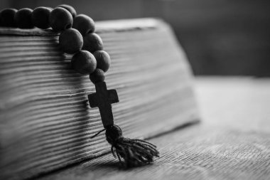 Tahta bir arka planda, kutsal İncil 'in üzerinde, üzerinde Hristiyan haçı bulunan ahşap dua boncukları yatıyor. Katolik ve Ortodoks inancı kavramı.