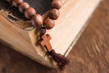 Tahta bir arka planda, kutsal İncil 'in üzerinde, üzerinde Hristiyan haçı bulunan ahşap dua boncukları yatıyor. Katolik ve Ortodoks inancı kavramı.