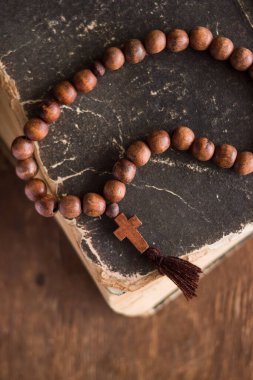 Tahta bir arka planda, kutsal İncil 'in üzerinde, üzerinde Hristiyan haçı bulunan ahşap dua boncukları yatıyor. Katolik ve Ortodoks inancı kavramı.