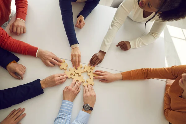 Büroangestellte mit mehreren Rassen montieren Holzpuzzles auf dem Schreibtisch, die Entwicklung und Erfolg symbolisieren. — Stockfoto