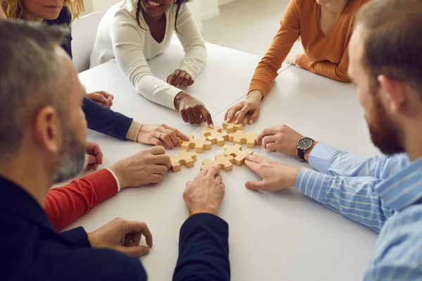 Vielfältiges Team von Geschäftsleuten sitzt am Tisch und fügt Puzzleteile zusammen — Stockfoto