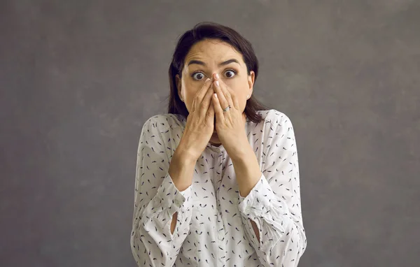 Scared young woman covering mouth with hand looking at camera studio shot — Stock Photo, Image