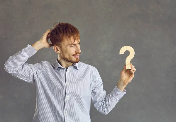 Serious thoughtful man looking at wooden question figure in hand studio shot