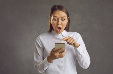 Genç bir kadın şok olmuş bir ifadeyle akıllı telefonunun ekranına bakıyor.