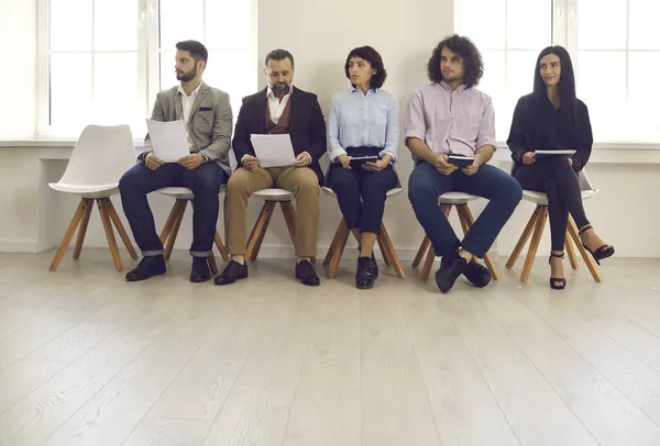 Kandidater med CV i händerna sitter på stolar i lobbyn och väntar på en intervju. — Stockfoto