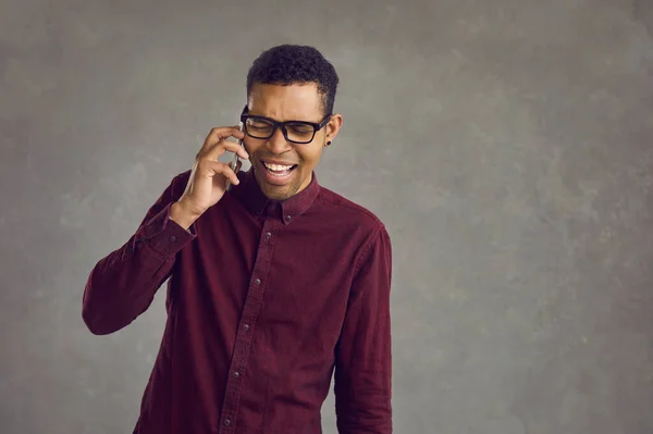 Gelukkige jonge Afro-Amerikaanse man voelt zich aangenaam opgewonden tijdens het praten aan de telefoon. — Stockfoto