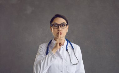 Kadın sağlık uzmanı ya da doktor işaret parmağını dudaklarına dayayıp sessizlik talep ediyor..