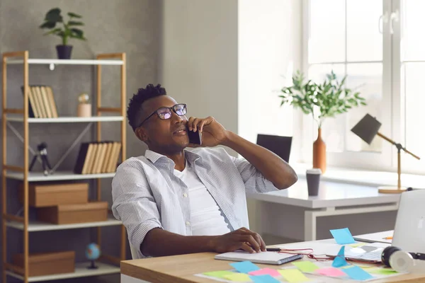 Jeune homme d'affaires afro-américain assis au bureau et parlant sur un téléphone portable — Photo