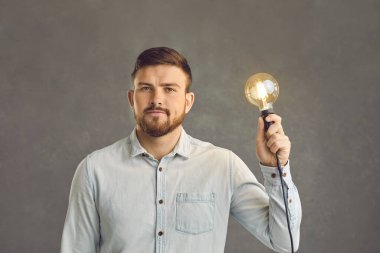 Ciddi bir özgüveni olan beyaz bir adam elinde yanan bir ampul stüdyosu fotoğrafı tutuyor.