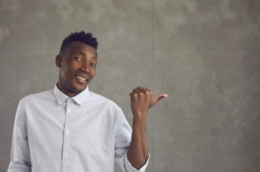 Mutlu genç siyahi adam parmağını gri beton duvardaki reklam alanına doğrultuyor.