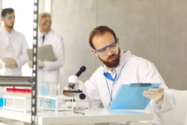 Retrato de cientista olhando para a área de transferência com trabalho de resultado de teste em laboratório — Fotografia de Stock