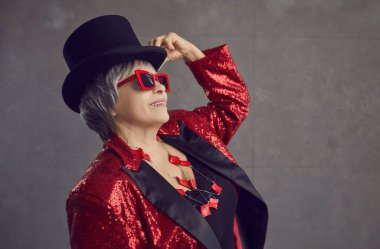 Şapkalı, havalı gözlüklü ve ceketli, stüdyoda poz veren genç ve mutlu bir bayan.