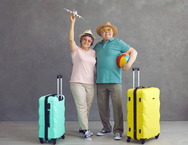 Studio porträtt av glada senior par i hattar och solglasögon med papper plan och resväskor — Stockfoto