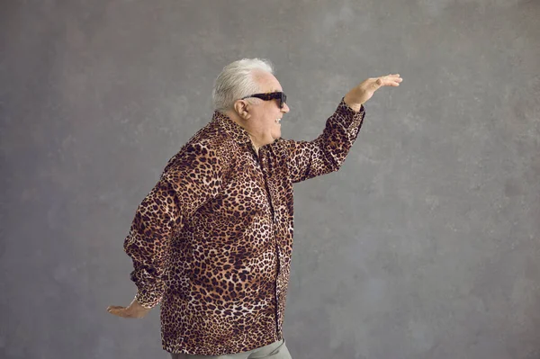 Vista laterale di divertente uomo anziano in camicia leopardata che balla in studio con sfondo grigio — Foto Stock