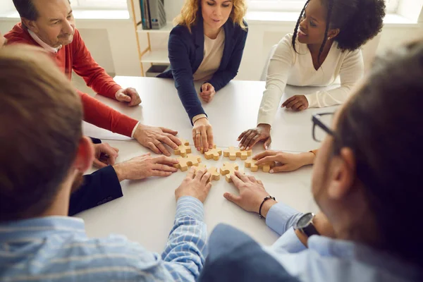 Glückliches, vielfältiges Business-Team sitzt am Bürotisch und fügt Puzzleteile zusammen — Stockfoto