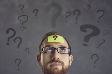 Gözlüklü bir iş adamının alnındaki bir kağıt parçasındaki soru işareti..