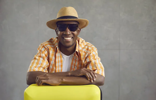 Studio portrait of happy black tourist in hat and sunglasses with his travel suitcase — Stock Photo, Image