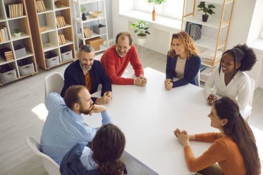 Ofis masasında oturup sohbet eden mutlu çalışanlar ve iş arkadaşları.