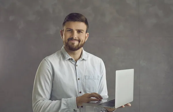Jistý usměvavý obchodní expert muž drží notebook stojící na zdi studia — Stock fotografie