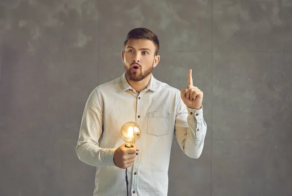 Překvapený muž přemýšlející a držící zářící žárovku má skvělý nápad studio shot — Stock fotografie