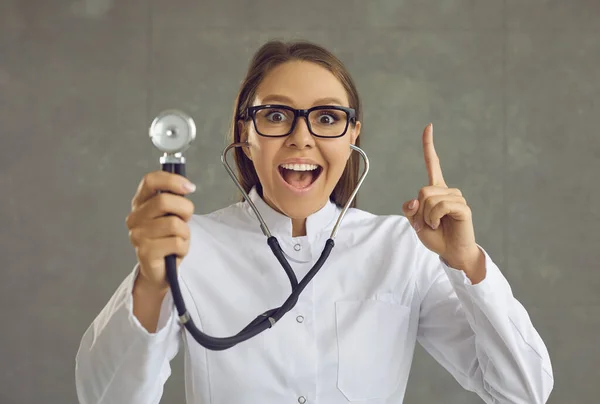 Портрет счастливого доктора со стетоскопом, показывающим пальцем вверх, пораженный великой идеей — стоковое фото