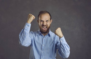 Sinirli, sinirli, sinirli, yumruklarını sıkmış ve çığlık atan bir adamın stüdyo portresi.