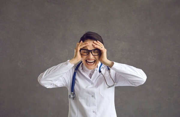 Stressed hospital nurse or doctor bursts into tears isolated on a grey background