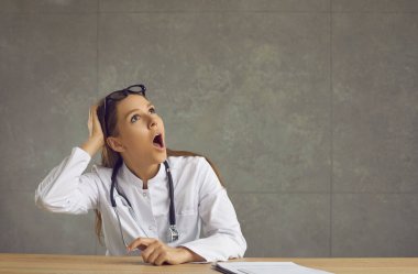 Şaşırmış doktor ya da hemşire masada oturuyor ve reklam sayfalarına bakıyor.