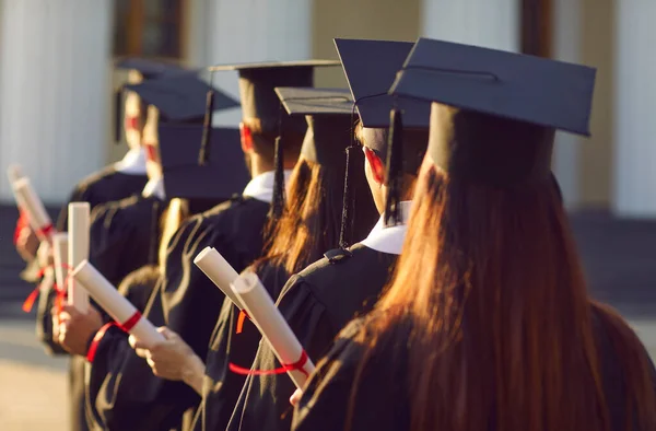 Skupina absolventů.Vysokoškolští absolventi line up hold degree award in graduation ceremony rear view — Stock fotografie