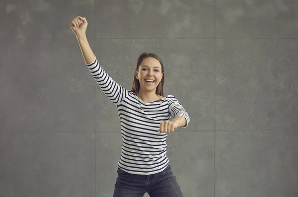 Šťastná mladá žena v pruhované top tanec gangnam styl proti šedé studio pozadí — Stock fotografie