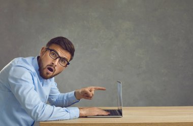 Masada oturan ve dizüstü bilgisayarın ekranını işaret eden gözlüklü adam şaşırdı.
