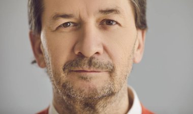 Gri stüdyonun arka planında kameraya bakan ciddi bir kıdemli adamın yakın plan portresi.