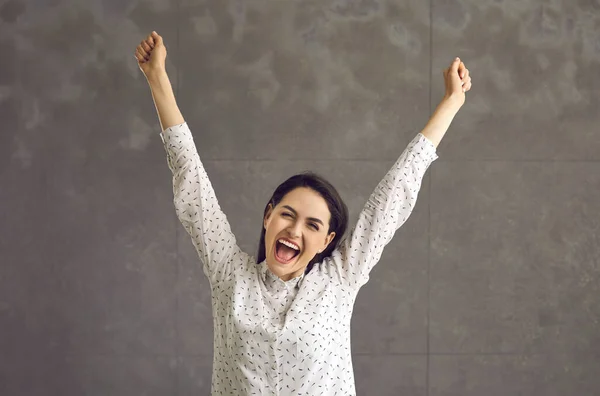 Mladá optimistická žena křičí a raduje se se zvednutou rukou studio shot — Stock fotografie