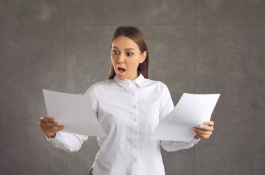 Gri arka planda izole edilmiş muhasebe hataları olan belgelere bakan şok olmuş bir kadın.