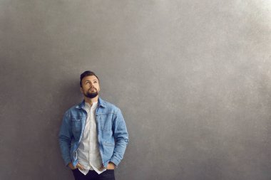 Gri stüdyo geçmişine karşı duran ve yukarı bakan düşünceli sıradan bir adam.