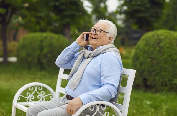 Homem sênior feliz falando no telefone celular enquanto sentado no banco no parque de verão verde — Fotografia de Stock