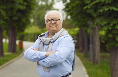Yeşil bir yaz parkında patikada duran kendinden emin yaşlı bir vatandaşın portresi.