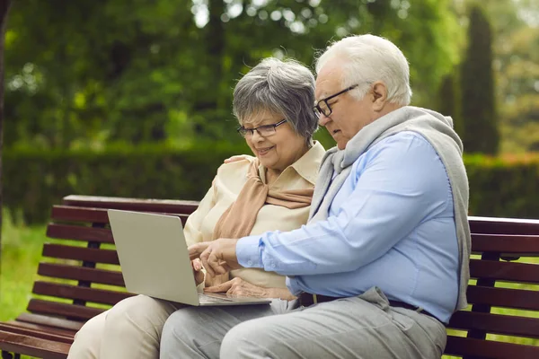 Heureux couple de personnes âgées utilisant un ordinateur portable tout en étant assis sur un banc de parc ensemble — Photo