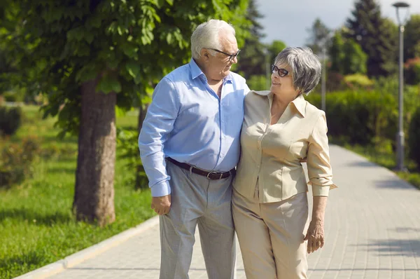 Porträt eines glücklichen Senioren-Paares, das an einem sonnigen Sommertag in einem grünen Park spaziert — Stockfoto