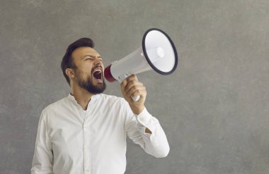 Gri arka planda duran megafona bağıran yetişkin beyaz bir adam.
